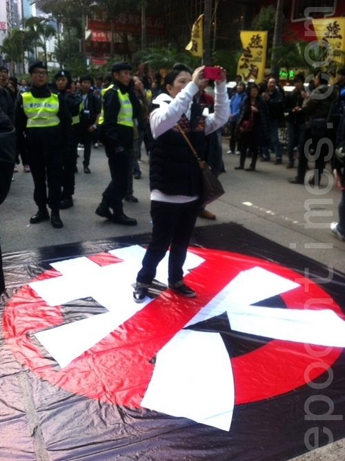 Женщина стоит на плакате с изображением перечёркнутого иероглифа, означающего «компартия». Протесты в Гонконге. Январь 2013 года. Фото: The Epoch Times Женщина стоит на плакате с изображением перечёркнутого иероглифа, означающего «компартия». Протесты в Гонконге. Январь 2013 года. Фото: The Epoch Times