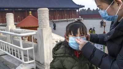 Мама надевает защитную маску на лицо дочери в Храме Неба в Пекине, Китай, 27 января 2020 года. Kevin Frayer/Getty Images