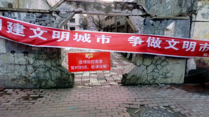 Некоторые жилые комплексы в районе Цяньцзинь снова закрыты, на двери висит большой горизонтальный баннер и предупреждающая табличка
