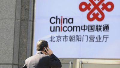 Офисный работник разговаривает по мобильному телефону на фоне логотипа China Unicom, партнёра Apple в Китае, 5 января 2012 года, Пекин. За коррупцию уже арестовано два руководителя компании. Фото: Liu Jin/AFP/Getty Images