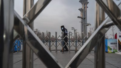 Охранник за шлагбаумом возле Национального стадиона, известного как «Птичье гнездо», который станет частью «пузыря», закрытого для посетителей и местных жителей, на зимних Олимпийских и Паралимпийских играх 2022 года в Пекине. Башня в Олимпийском парке в Пекине, Китай, 19 января 2022 года. (Kevin Frayer/Getty Images)